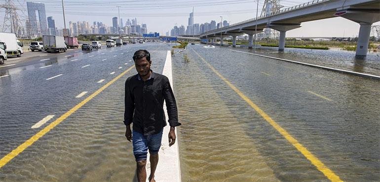 A man walks along a road barrier among floodwater caused by heavy rain on Sheikh Zayed Road highway in Dubai, United Arab Emirates, Thursday, April 18, 2024. (AP Photo/Christopher Pike)