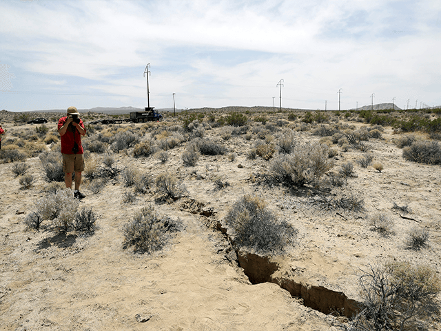 In this July 7, 2019 file photo, a visitor takes a photo of a crack in the ground following recent earthquakes near Ridgecrest, Calif. Scientists say the earthquakes that hammered the Southern California desert near the town of Ridgecrest last summer involved ruptures on a web of interconnected faults and increased strain on a major nearby fault that has begun to slowly move. (Marcio Jose Sanchez, AP)