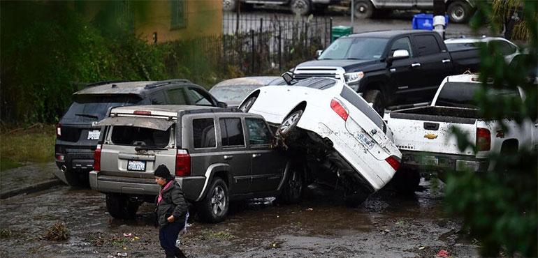 A woman walks by cars damaged from floods during a rain storm Monday, Jan. 22, 2024, in San Diego. (AP Photo/Denis Poroy)