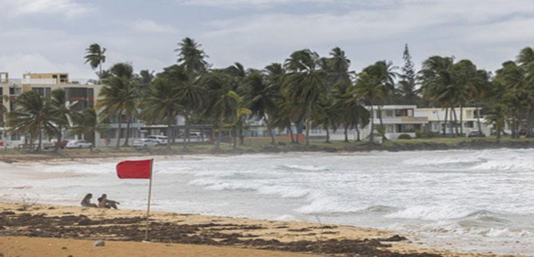Tourists sit on La Pared beach as Tropical Storm Ernesto passes by Luquillo, Puerto Rico, Tuesdasy, Aug. 13, 2024. (AP Photo/Alejandro Granadillo)