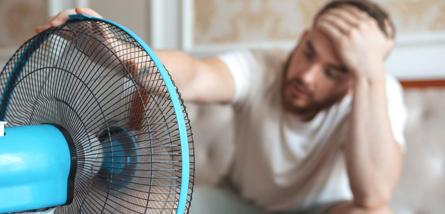 Young bearded man using electric fan at home. (EugeneEdge via Shutterstock)