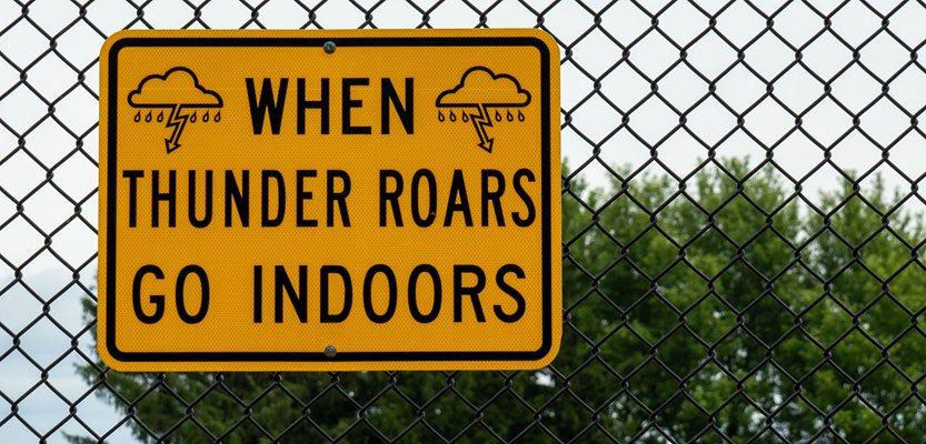 A yellow and black sign says "When Thunder Roars Go Indoors", reminding people to seek shelter in bad weather. (Kimberly Boyles via Shutterstock)