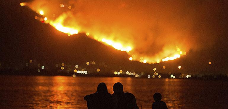 In this Aug. 9, 2018, file photo, a family sits along the shore of Lake Elsinore as they watch the Holy Fire burn in the distance in Lake Elsinore, Calif. ( Patrick Record, AP)
