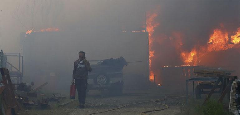 A man carries a fire extinguisher and seeks on the phone while a metalworking warehouse burns in Sever do Vouga, a town in northern Portugal that has been surrounded by forest fires, Monday, Sept. 16, 2024. (AP Photo/Bruno Fonseca)
