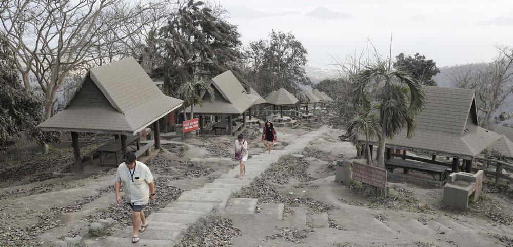 People walk along a park covered in volcanic-ash at a town near Taal volcano in Tagaytay, Cavite province, southern Philippines on Sunday Jan. 19, 2020. (AP Photo/Aaron Favila)