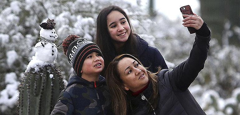 "It's the first time we've seen snow the desert," says Mayra Vasquez who brought Valeria Luzania, 11, and MarcoDario Luzania, 8, to Saguaro National Park East on January 02, 2019. The kids built a snowman and the trio took a selfie with their creation. (Mamta Popat /Arizona Daily Star via AP)