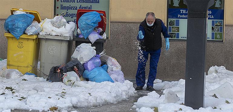 A man sprinkles salt on snow and ice next to uncollected overflowing garbage bins in Madrid, Spain, Tuesday, Jan. 12, 2021. Much of Spain is struggling to return to normality three days after a 30-hour-long record snowfall that was then hardened by record-low temperatures. (Paul White, AP)