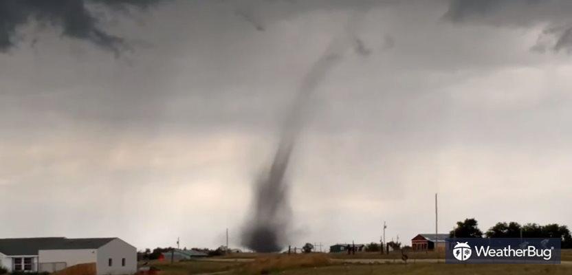 A landspout spins close to buildings under dark, cloudy skies