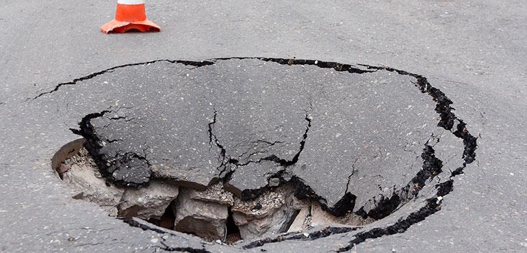 Deep sinkhole on a street city and orange traffic cone. (rbkomar via Shutterstock)