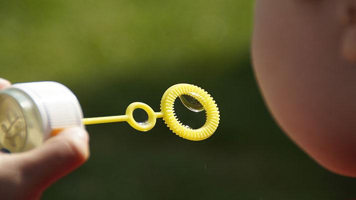 A close up of the back of a child's head with their hand holding a yellow bubble wand (Image by M W from Pixabay)