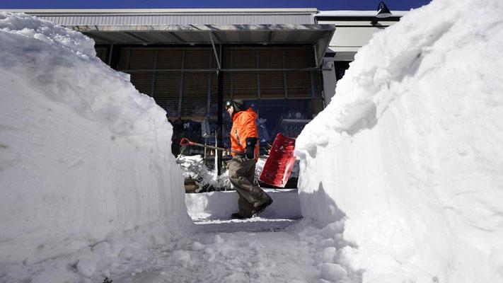 A Cohasset, Mass., resident carries a snow shovel past a snow bank on a sidewalk, Sunday, Jan. 30, 2022, in Scituate, Mass. Gusty winds and falling temperatures plunged the East Coast into a deep freeze as people dig out from a powerful nor’easter that dumped mounds of snow, flooded coastlines and knocked power out. (AP Photo/Steven Senne)